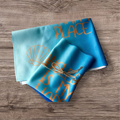 alt=“Quick-drying and absorbent microfibre tea towel with ‘Anglesey is my happy place’ slogan – ideal for beach lovers and coastal kitchens”