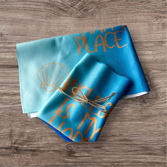 alt=“Quick-drying and absorbent microfibre tea towel with ‘Anglesey is my happy place’ slogan – ideal for beach lovers and coastal kitchens”