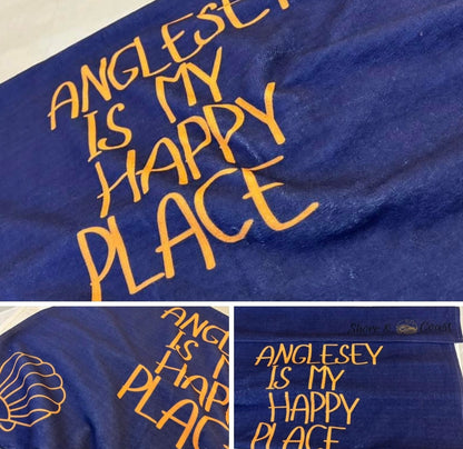alt=“Navy microfibre beach towel with cotton loops featuring the slogan ‘Anglesey is my happy place’ in bold orange text – quick-drying, absorbent, and perfect for the coast”