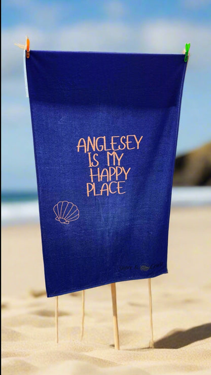 alt=“Navy microfibre beach towel with cotton loops featuring the slogan ‘Anglesey is my happy place’ in bold orange text – quick-drying, absorbent, and perfect for the coast”