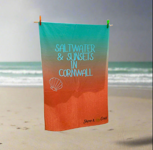 alt=“Lightweight, quick-drying mint and orange microfibre beach towel with the slogan ‘Saltwater & Sunsets in Cornwall’ in bold white text – perfect for beach days”