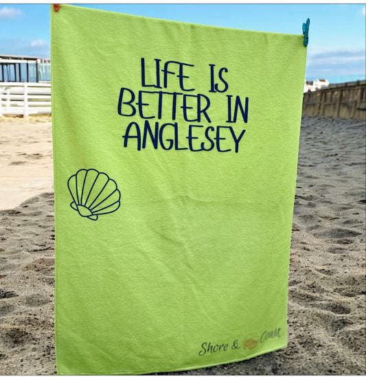 alt=“Lime green microfibre beach towel with cotton loops and the slogan ‘Life is better in Anglesey’ in bold yellow text – ultra-absorbent, quick-drying, and perfect for seaside adventures”