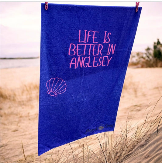 alt=“Purple microfibre beach towel with cotton loops and the slogan ‘Life is better in Anglesey’ in bold pink text – ultra-absorbent, quick-drying, and perfect for seaside adventures”